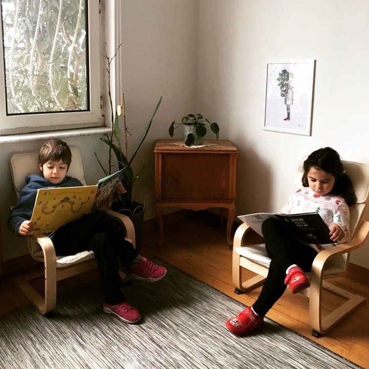 Pencere önündeki küçük koltuklarda kitap okuyan iki çocuk